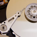 An image of the mechanical parts of a hard disk drive or HDD that features a rotating metallic magnetic disk and a magnetic read-write head.